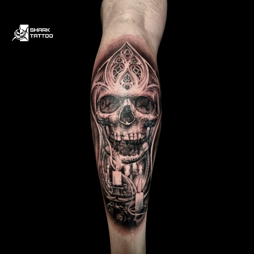 Dieses beeindruckend schöne Tattoo zeigt einen detaillierten Totenschädel, der mit kunstvollen gotischen Elementen verziert ist. Das filigrane Design an der Spitze verleiht einen majestätischen Touch, während die darunterliegenden Kerzen eine geheimnisvolle und symbolische Atmosphäre schaffen, die Themen wie Leben, Tod und den Lauf der Zeit widerspiegeln. Perfekt platziert und mit größter Präzision gestochen, ist dieses Kunstwerk eine ausdrucksstarke Darstellung von dunkler Eleganz und Individualität.

Bereit, deine dunkle Seite mit einem Meisterwerk wie diesem auszudrücken? Buche jetzt auf www.sharktattoo.de oder rufe uns an unter +49 174 4552303. Lass uns ein Design schaffen, das deine Seele widerspiegelt! 🖤✨